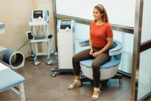 A woman sits on a medical device chair in a clinic setting.